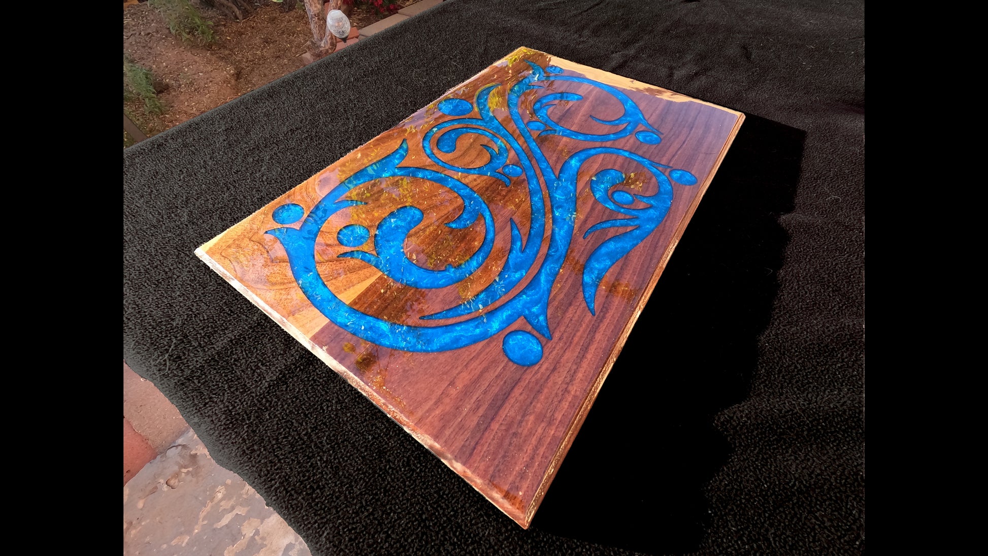 Corner view of a blue epoxy script style inlaid into a 20X13X3/4" piece of walnut and finished with a glasslike smooth epoxy finish.