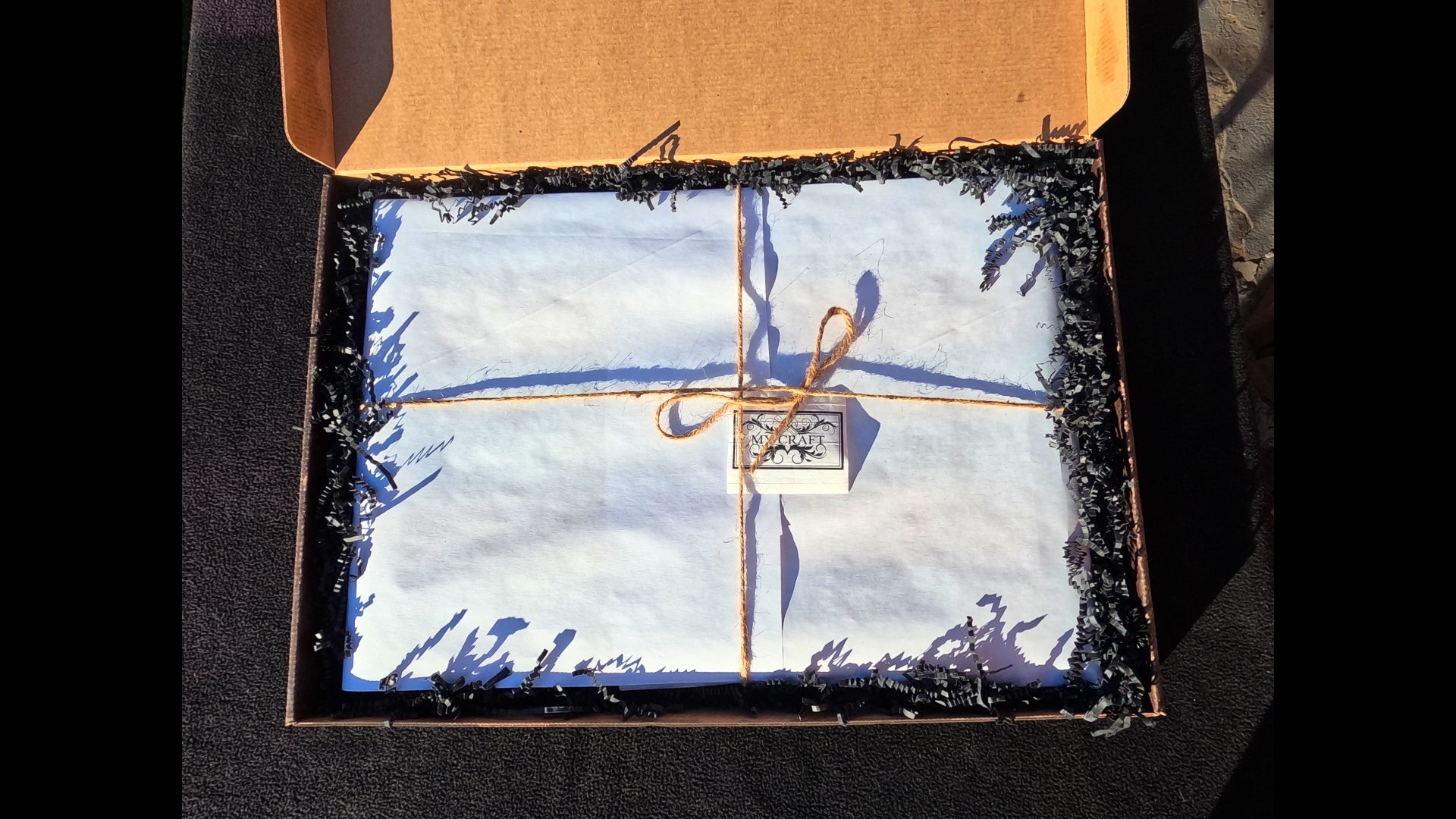 Top view of the custom-made packaging with the board wrapped in a protective paper tied off with twine string and packed with black string paper for gift ready aesthetics.