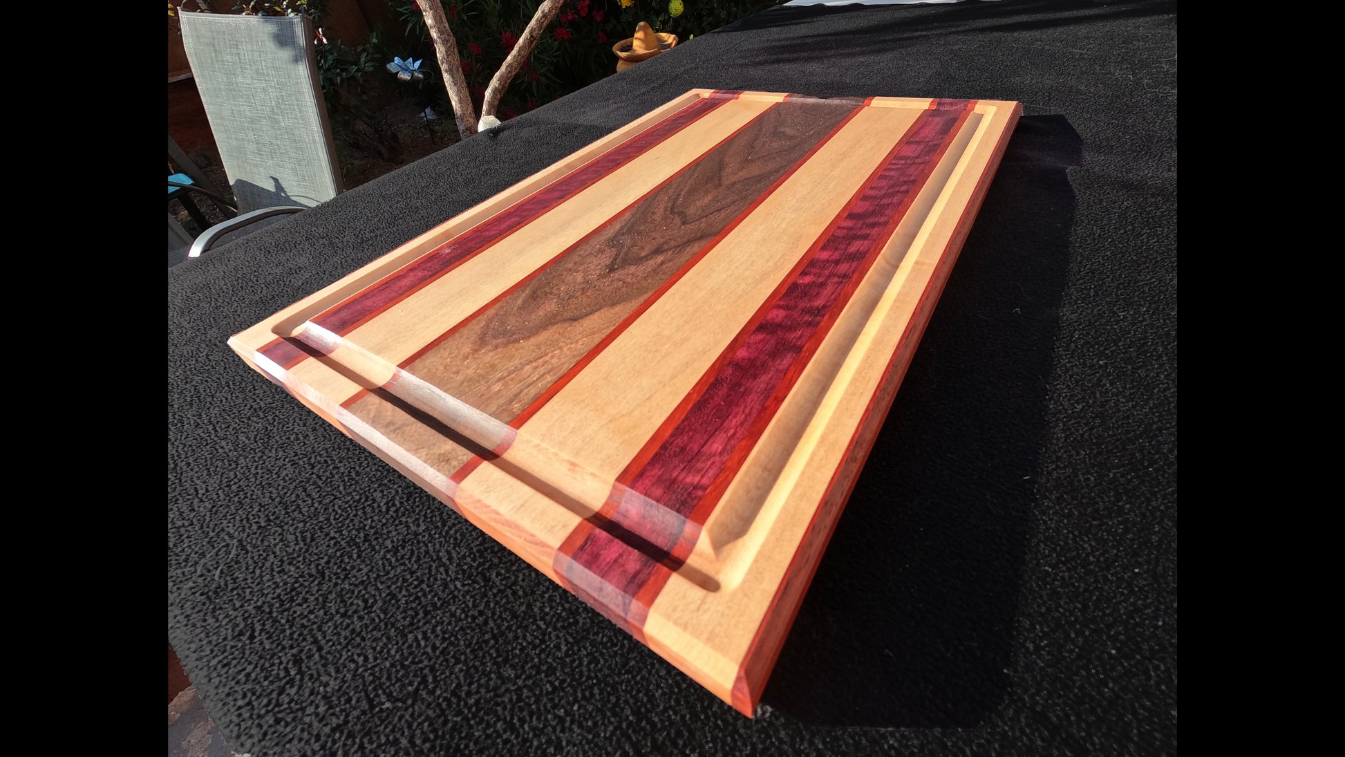 Front corner view of the Slice of life cutting board with striped pattern, featuring Maple, walnut, purple heart, and padauk hardwoods.