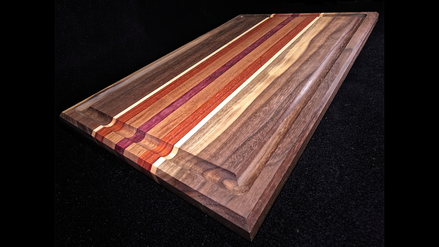 lower front corner view of the Board to death stripped pattern Cutting board, featuring Walnut, maple, padauk, African mahogany, and purple heart hardwoods.